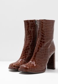 Bottes courtes marron brillantes avec un motif texturé crocodile, bout carré et talon épais, dotées d'une fermeture éclair latérale.