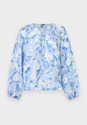 Lys blå bluse med lange ermer, hvit og blå blomsterprint, rynket halslinning med nøkkelhull og knytebånd, og elastiske mansjetter.