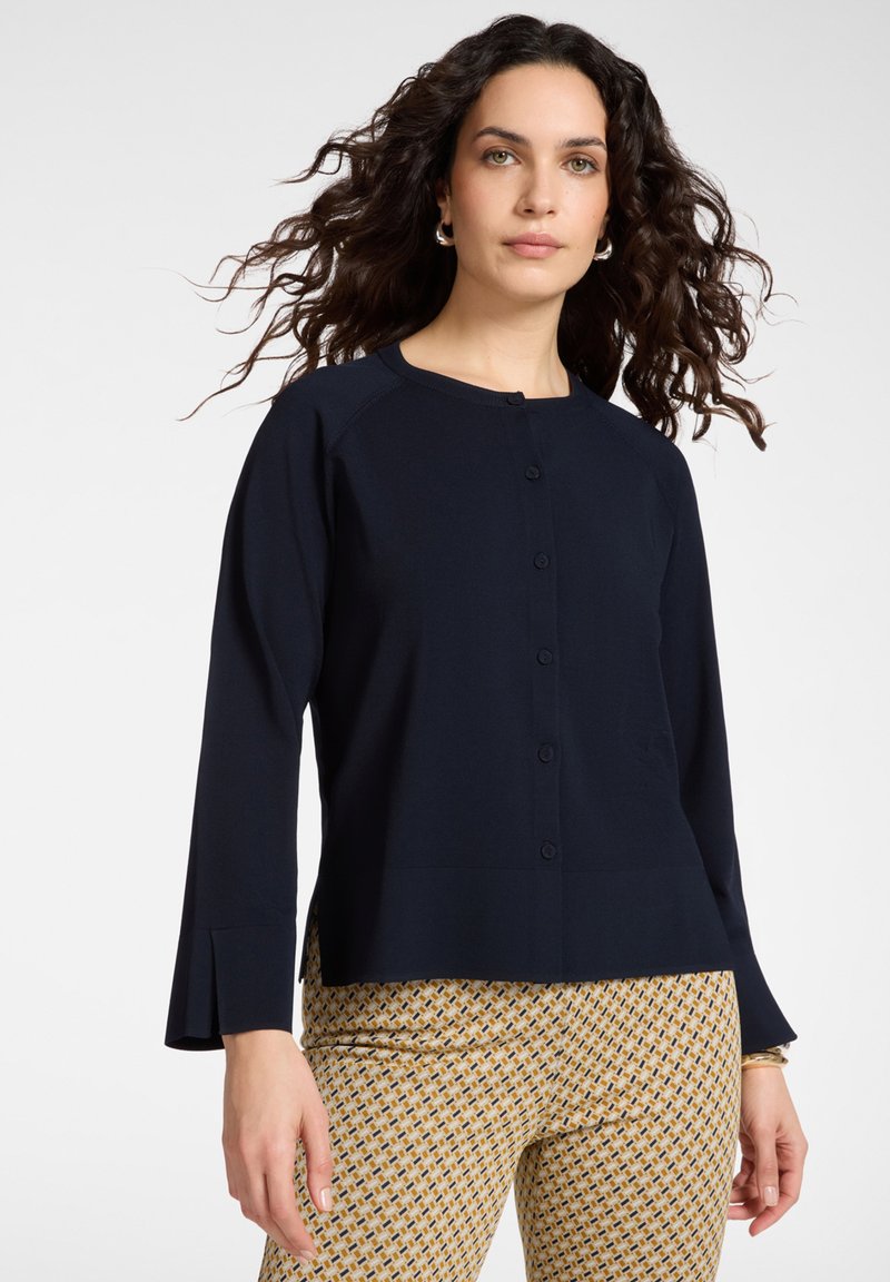 Cardigan blu navy a maniche lunghe con scollo rotondo e chiusura frontale con bottoni. Presenta maniche aderenti e un orlo dritto.