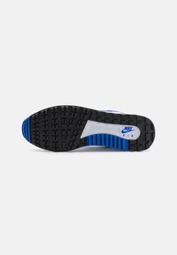 Černá gumová podrážka s hlubokými vzory, bílá mezipodešev s modrými akcenty a logo Nike Air poblíž paty.