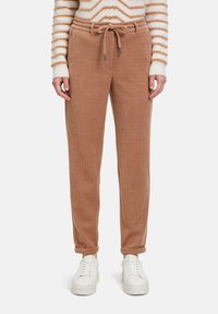 Bruine corduroy joggers met een trekkoord taille, tapered fit enopgerolde manchetten. Gecombineerd met witte sneakers voor contrast.