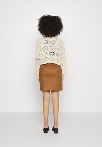 Jersey de crema tejido a crochet con un corte relajado, combinado con una falda de ante marrón. Unos zapatos negros de tacón cuadrado completan el conjunto.