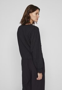 T-shirt preta de manga longa com ombros bufantes e bainha cropped. Textura suave com punhos elásticos; design minimalista sem padrões.