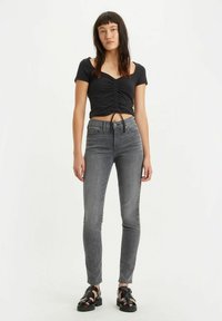 Top negro corto con frunce en el frente, combinado con jeans gris de cintura alta, con un ajuste ceñido y diseño clásico de cinco bolsillos. Sandalias negras de tiras.