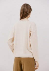 Lichtroze lange mouwtop met een losse pasvorm, voorzien van een ronde halslijn en subtiele geribbelde textuur. Gepaard met olijfgroene broeken.