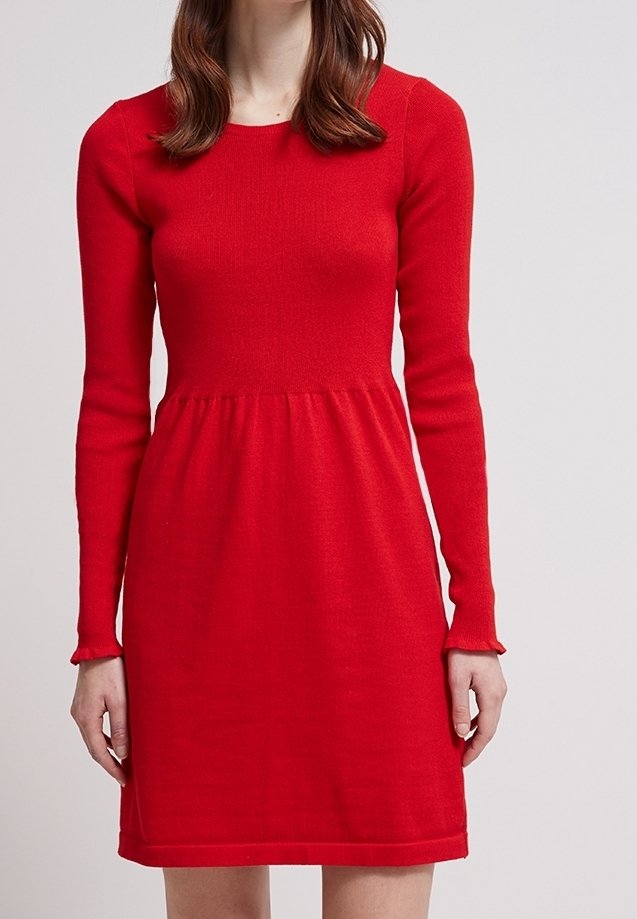 Abito in maglia rossa con busto aderente, maniche lunghe e gonna svasata. Il tessuto ha una consistenza liscia con pochi dettagli.