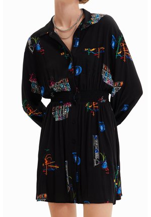 Schwarzes langärmeliges Kleid mit bunten abstrakten Mustern und Text, mit Knopfleiste vorne und elastischem Taillenbund, getragen mit geschichteten silbernen Ketten.