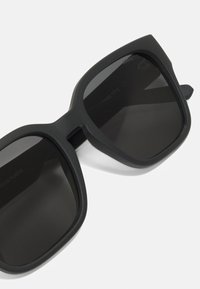 Occhiali da sole neri realizzati in plastica riciclata, con finitura opaca, montatura rettangolare e lenti scure. Accentuati da un branding minimale.