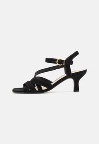 Sandali con tacco in suede nero, caratterizzati da cinturini incrociati, una fascia alla caviglia con una fibbia dorata e un tacco di altezza media per maggiore stabilità.