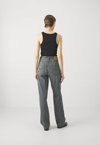 Black tank top paired with gray wide-leg jeans featuring a high waist, distinctive stitching, and a leather patch on the back waistband.