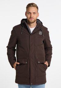 Brun parka-jakke med lynlås og trykknaplukning, med hætte, to forlommer og et logo-patch på brystet. Blød tekstur.