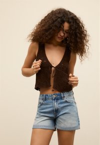 Ruskea virkattu toppi, jossa on V-aukko ja solmittava etusuunnittelu, yhdistettynä vaaleansinsisiin denim-shorteihin, joissa on käänteinen helma.