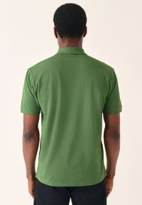 Zöld rövid ujjú póló, sima anyagból készült. Gallérral rendelkezik, visszafogott kialakítással, további minták vagy díszítések nélkül.