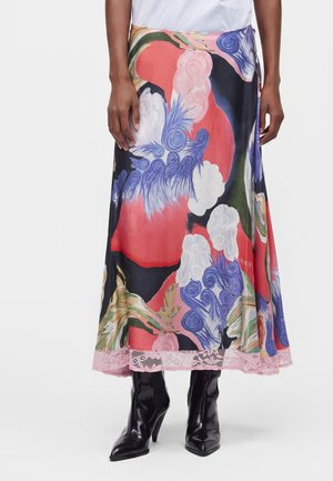 Jupe avec des motifs abstraits rouges, bleus, blancs, verts et roses, bordure en dentelle à l'ourlet, portée avec des bottines noires à talons et un haut blanc.
