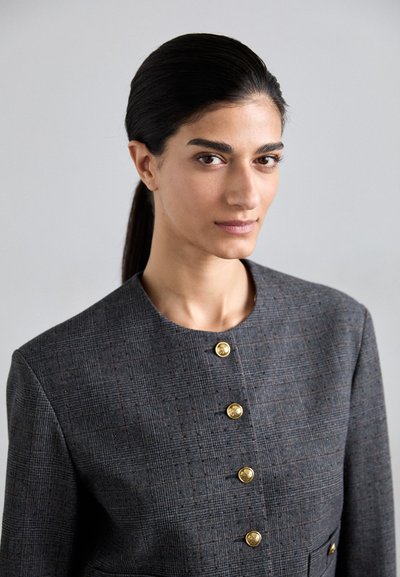 Grijze geblokte blazer met een ronde halslijn, vijf gouden knopen en een gestructureerde stof. Opvallend door de stevige schouders en een getailleerde pasvorm.