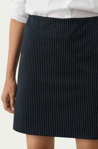 Tamnoplavi suknja s prugama u uspravnom kroju, izrađena od meke tkanine. Ima fine bijele pruge i glatku teksturu. Porub završava iznad koljena.