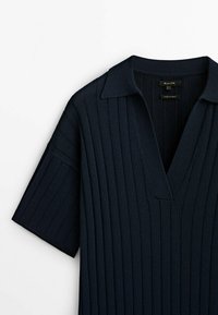 Navy blue short-sleeve polo shirt with ribbed texture, V-neckline, and a flat collar. Features clean lines and minimalist design.