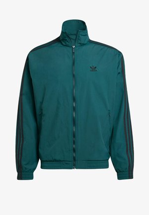 Türkiz színű cipzáros dzseki magas gallérral, fekete Adidas logóval és fekete három csíkkal az ujjakon; elasztikus mandzsetták és alsó szegély.