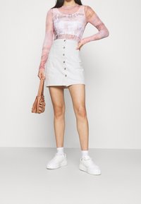 Pitkähihainen, läpikuultava paita, jossa on vaaleanpunainen ja valkoinen kuvio; valkoinen farkku mini-hame etupainikkeilla; pieni ruskea käsilaukku; valkoiset platform-tossut.