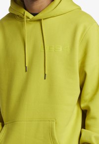 Limegrön hoodie i slätt tyg har en framficka, dragsko i huvan och en präglad "DC94"-logotyp på bröstet.