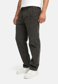 Corduroy pants in dark gray, featuring a straight-leg design, vertical ridges, front pleats, and a subtle brand tag on the waistband.
