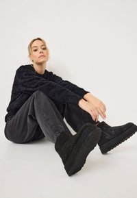 Bottines noires avec des dessus texturés ornés d'accents scintillants, une semelle épaisse et un col rembourré, associées à un pantalon gris ample et un pull.