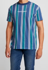 Tričko s krátkým rukávem se svislými modrými a tyrkysovými pruhy, s bílými akcenty a textem "NIGHT ADDICT" přes hruď.