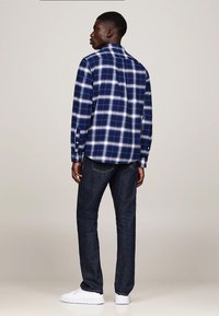 Camicia in flanella a quadri blu e bianca con maniche lunghe, polsini a bottoni e orlo curvo, abbinata a jeans in denim scuro e sneakers bianche.