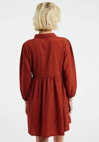 Röd klänning med svarta prickar, långa ärmar, knäppt krage, skrynklig midja och en flödande kjol. Mjuk tyg med en slät yta.