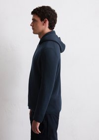 Navy blue hooded sweatshirt with a textured fabric, side zipper, and long sleeves, worn by a person facing left against a neutral background.