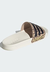 Pantofle Adidas typu slide s krémově zbarvenou podrážkou, páskem s leopardím potiskem a třemi černými pruhy, vybavené texturovanou podrážkou pro lepší přilnavost.