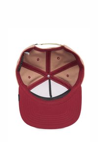 Red fabric cap with a beige interior, featuring a curved peak, stitched detailing, and ventilation holes. Label present on the side.