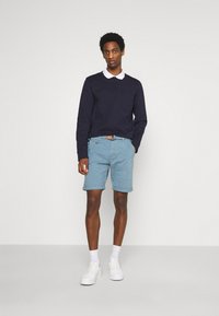 Camisa de manga larga navy con un color blanco en el collar, pantalones cortos azul claro y zapatillas blancas. Diseño casual con un bolsillo frontal en la camisa.