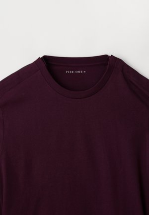 Camiseta de crewneck de color púrpura oscuro con mangas cortas, colocada plana, mostrando la etiqueta del cuello interior "PIER·ONE" sobre un fondo blanco.