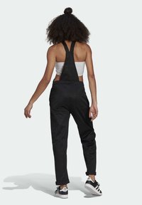 Černé denimové overall s nastavovacími pásky, zúženými nohavicemi a předními kapsami, v kombinaci s bílým crop topem a černými teniskami.