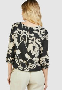 Schwarze Bluse mit cremefarbenem Blumenmuster, dreiviertel Ärmel, runder Ausschnitt und einem kleinen Schlitz im Rücken. Leichter Stoff.