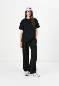 T-shirt noire oversized, pantalon noir ample et baskets grises. Casquette violette claire avec un design brodé. Couleurs unies et formes simples.