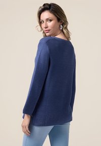 Pulover tricotat de culoare bleu marin, cu un decolteu larg și margine ondulată. Țesătura are un model texturat și dispune de mâneci lungi.