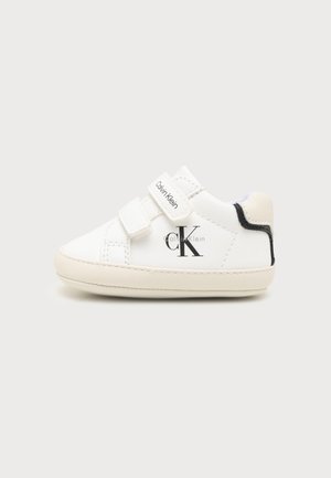 Witte babysneaker met twee klittenbandsluitingen, Calvin Klein-logo aan de zijkant en op de band, lichtbeige zool en zwarte rand bij de hiel.