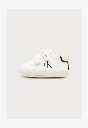 Biała dziecięca tenisówka z dwoma paskami na rzep, logo Calvin Klein po boku i na pasku, jasnobeżowa podeszwa oraz czarne wykończenie na pięcie.