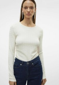 Langermet, teksturert hvit topp med rund hals, kombinert med mørkeblå jeans med frontlommer og knappestolp.