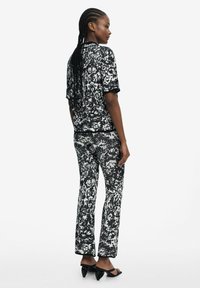Black and white patterned shirt and pants set featuring short sleeves and a relaxed fit. The fabric has a textured appearance. Black heeled sandals.