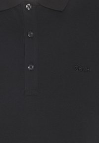 Schwarzes Polohemd aus strukturiertem Stoff, mit einer Knopfleiste aus drei Knöpfen, geripptem Kragen und einem gestickten "HUGO"-Logo auf der Brust.