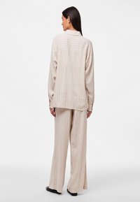 Completo beige a righe composto da un top a maniche lunghe dal taglio morbido e pantaloni a gamba larga, entrambi con righe verticali e una consistenza soffice.