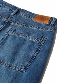 Denim-Jeans in Mittelblau mit einer abgetragenen Textur, ausgestattet mit orangenen Nähten und einem Leder-Label an der Taille. Zwei Gesäßtaschen.