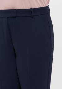 Marineblaues Hosen mit einer glatten Textur, ausgestattet mit einem Bund mit Gürtelschlaufen und Seitentaschen, im schmalen Schnitt gestaltet.