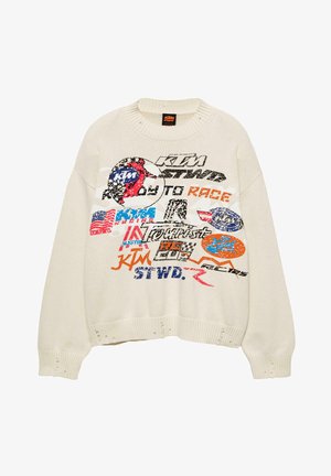 Pull en tricot beige avec des logos et du texte de course KTM multicolores, présentant des trous usés aux poignets et à l'ourlet.