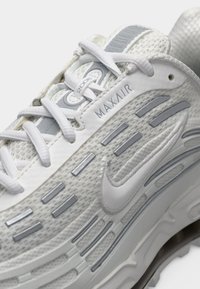 Gros plan d'une basket Nike Max Air 2006 blanche et grise avec lacets et semelle texturée visibles.