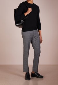 Musta neulepusero, harmaat ruudulliset räätälöidyt housut ja mustat lenkkarit. Henkilöllä on musta nahkainen reppu. Sileä pinta ja moderni istuvuus.