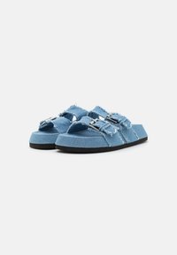 Blå denim slidesandaler med två breda remmar, silvriga spännen och fransade kanter. Tjock svart gummisul för ökad stabilitet.